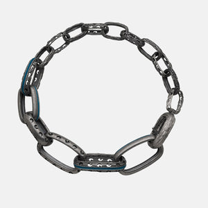 Circular chain bracelet in carved oxidized silver and bright blue inlay arranged on a soft grey canvas.