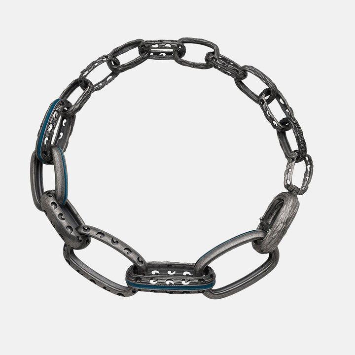Circular chain bracelet in carved oxidized silver and bright blue inlay arranged on a soft grey canvas.