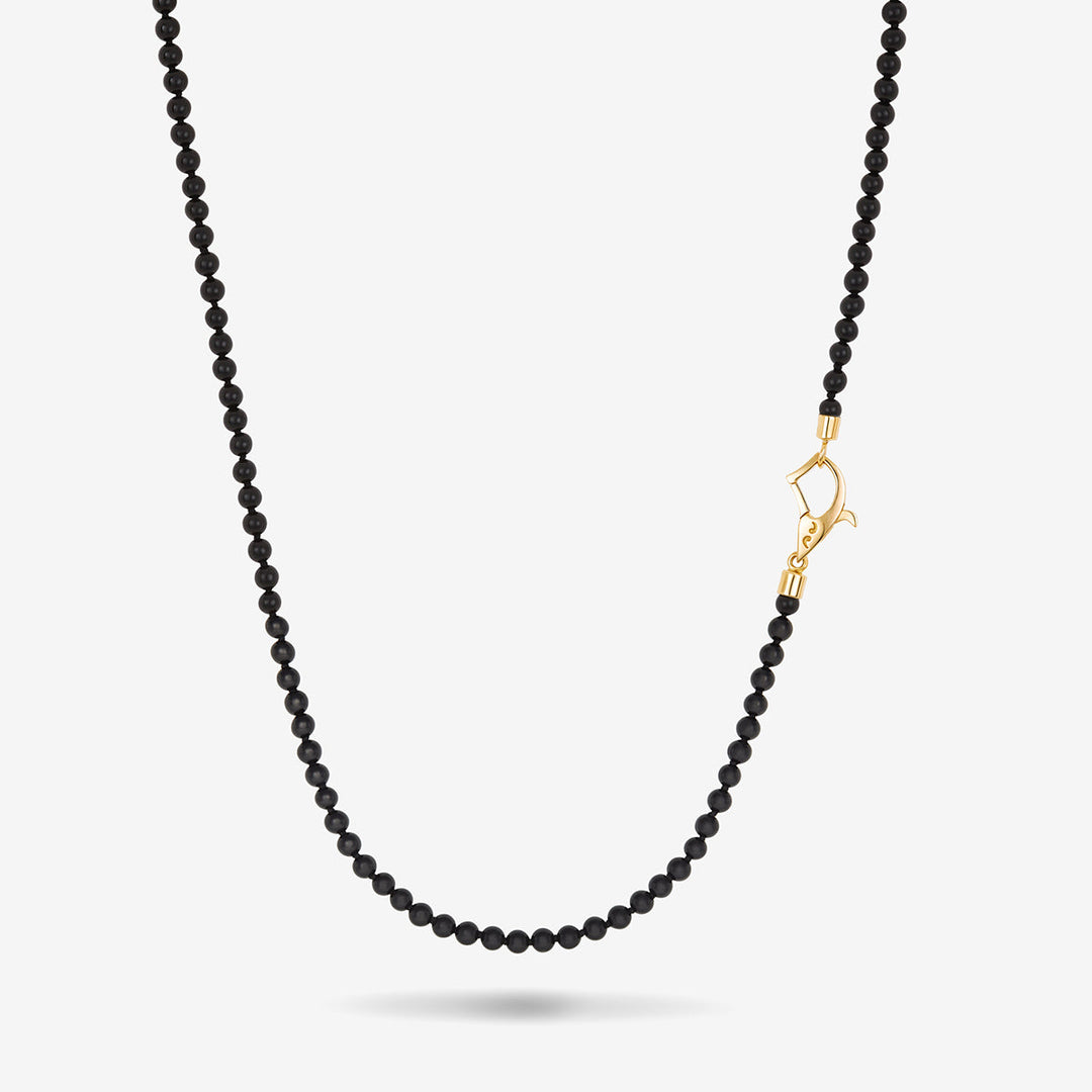 Beaded necklace in solid black stones and an asymmetrical yellow gold clasp set against a bright studio backdrop.