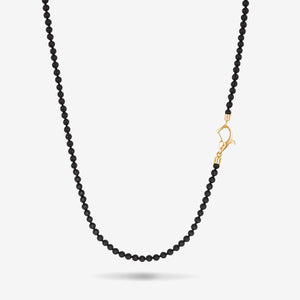 Beaded necklace in solid black stones and an asymmetrical yellow gold clasp set against a bright studio backdrop.