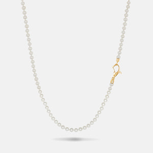 Beaded necklace in smooth white stones and a side-oriented yellow gold closure resting on a soft neutral background.