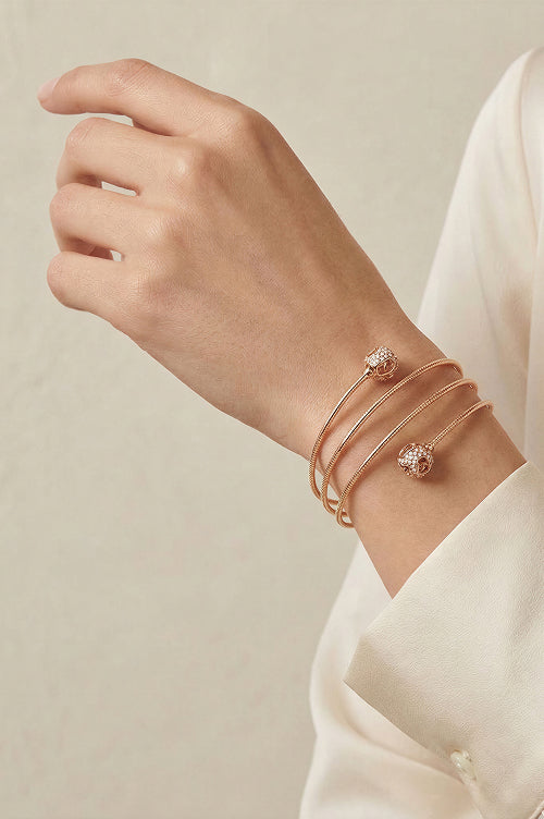 Close-up of a wrist wearing two open gold-tone bangles with decorative ends.