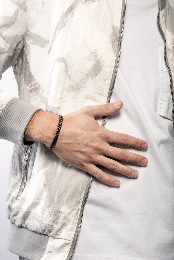 Male model wearing the MARCO DAL MASO Flaming Tongue Cuban Link Bracelet in rose gold vermeil and oxidized silver, featuring a slim interlocking chain design, styled with a light patterned jacket.