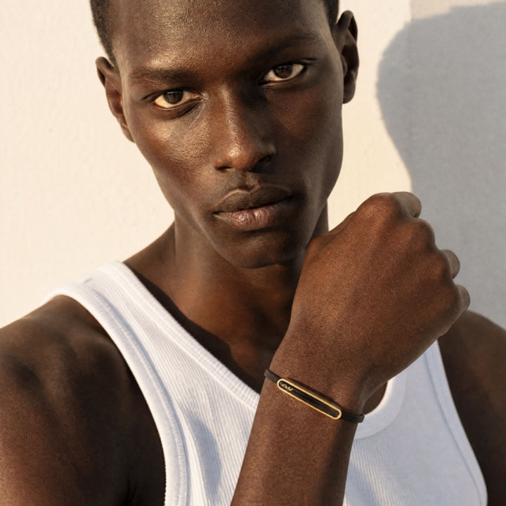 Model wearing the Frame Enamel ID Leather Bracelet in 18K yellow gold, featuring a sleek gold ID detail on a dark leather strap.