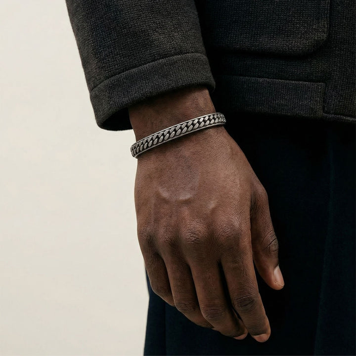 Model wearing the MARCO DAL MASO Ulysses Wide Chain Cuff in oxidized silver, featuring an intricate chain-link pattern and sculptural design, styled with dark clothing in a close-up wrist portrait.