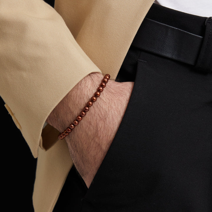 Cropped frame of umber bead strand touching a beige blazer cuff.