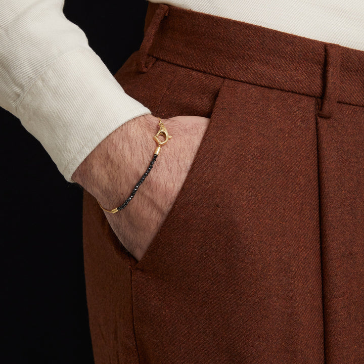 Close-up of black bead bracelet resting against brown trousers.